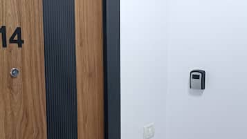 Une porte en bois portant le numéro 14 et munie d’un trou de serrure, un panneau à rayures verticales et un mur blanc avec une poignée de porte.