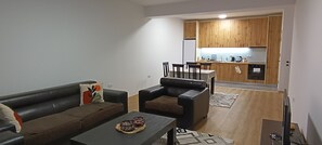 A modern living room with a sofa, a coffee table, and a dining area with chairs and a table.