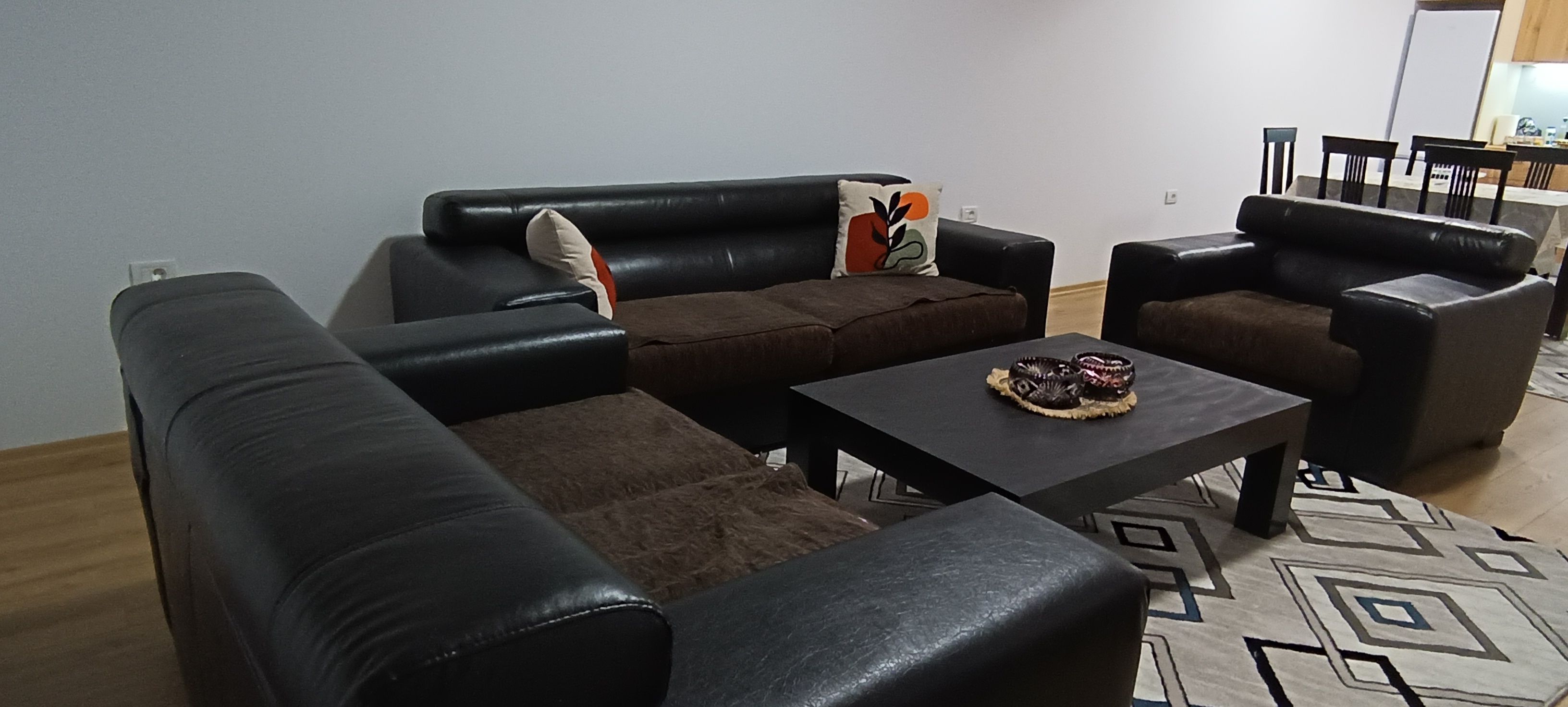 Een woonkamer met een bank, twee fauteuils, een salontafel en een kamerkleed met een patroon.