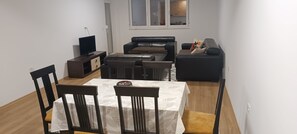 A compact living space with a dining table, chairs, a sofa, a TV, and a small cabinet.