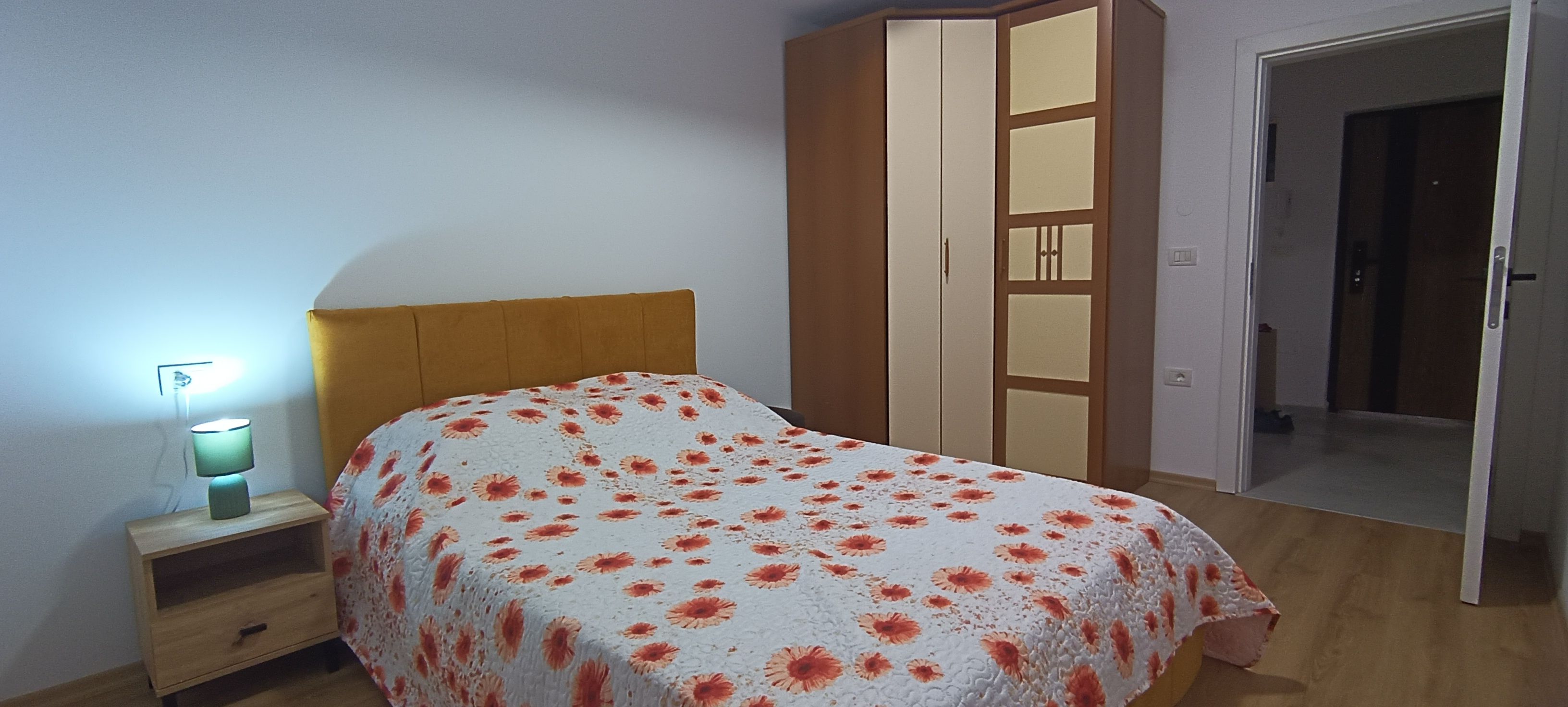 Un dormitorio con una cama, una mesita de noche, un armario y una puerta que da a otra habitación.
