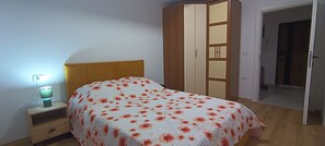 Un dormitorio con una cama, una mesita de noche, un armario y una puerta que da a otra habitación.