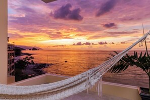 Un hamac sur un balcon donnant sur un coucher de soleil sur l’océan.