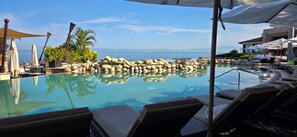 A poolside area with lounge chairs, a clear pool, and a view of the sea. - Oceanfront Studio in a 5 star Garza Blanca Resort, Puerto Vallarta, Mexico (Puerto Vallarta)