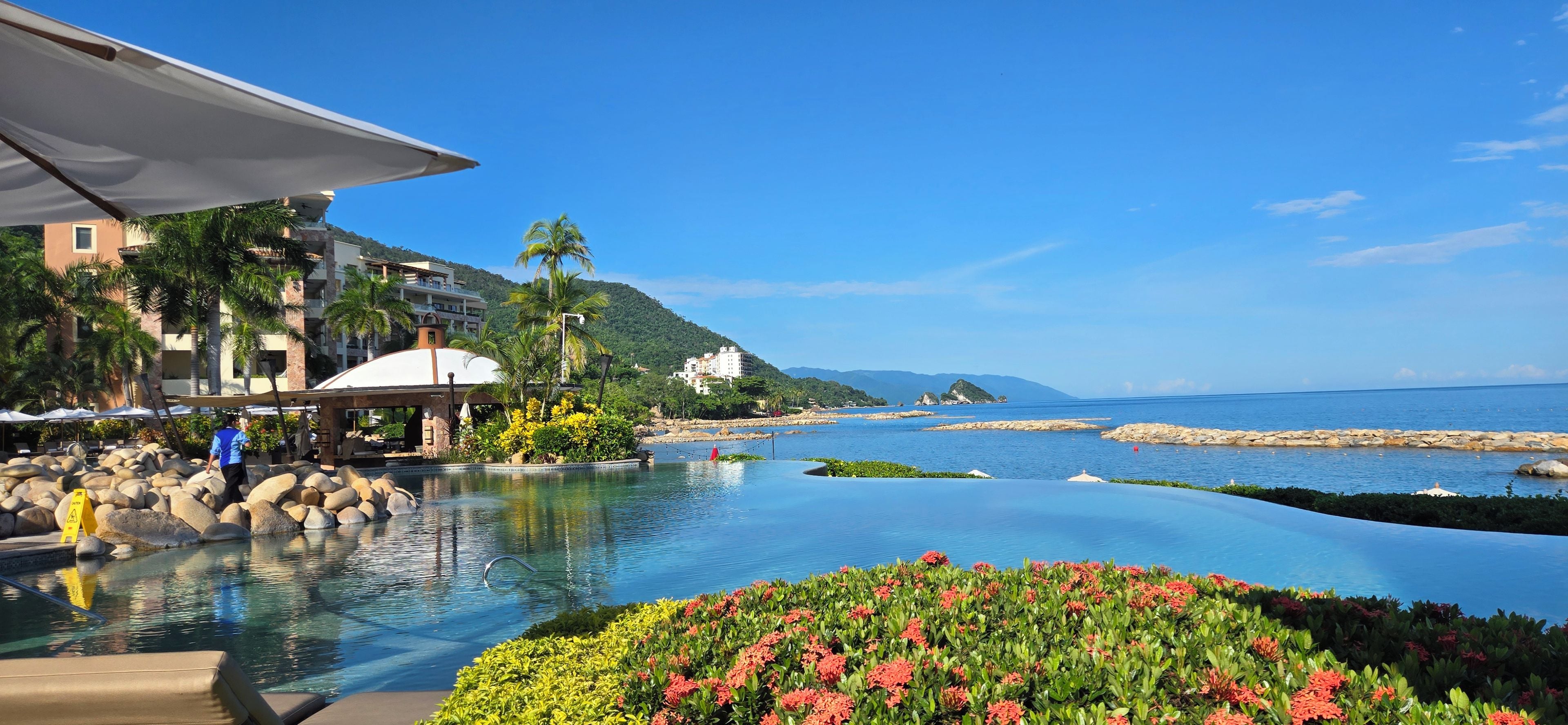 A resort with a pool, palm trees, and a view of the sea.
