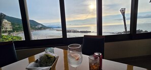 Un tavolo con bevande, uno spuntino e una lattina, vista su una spiaggia e l'oceano attraverso ampie finestre.