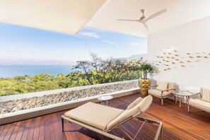 Un balcone con vista sul mare, una ventola a soffitto e un'area salotto con un tavolo.