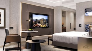 A modern hotel room with a large bed, a TV mounted on the wall, a small round table with a bowl of fruit, and a chair. - Doubletree By Hilton Diyarbakir (Diyarbakir)