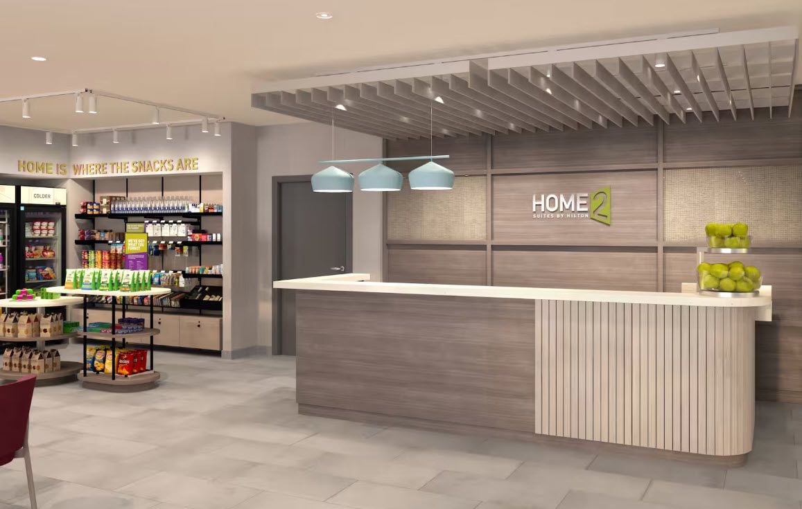A modern hotel lobby with a reception desk, snack area, and a sign reading 'HOME 2'.