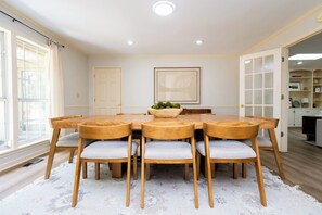 Ein Esszimmer mit einem runden Holztisch, sechs Stühlen, einem weißen Teppich und einem gerahmten Bild an der Wand.