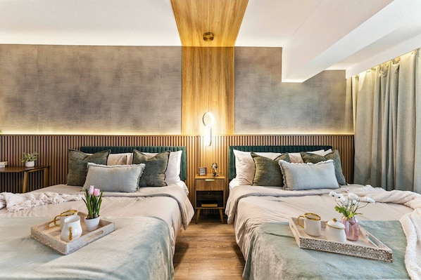 A hotel room with two beds, a wooden ceiling, a nightstand with a lamp, and a tray with a pitcher and flowers.