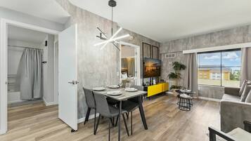 A modern living room with a dining area, a yellow accent wall, a large window with a view, and a grey sofa.