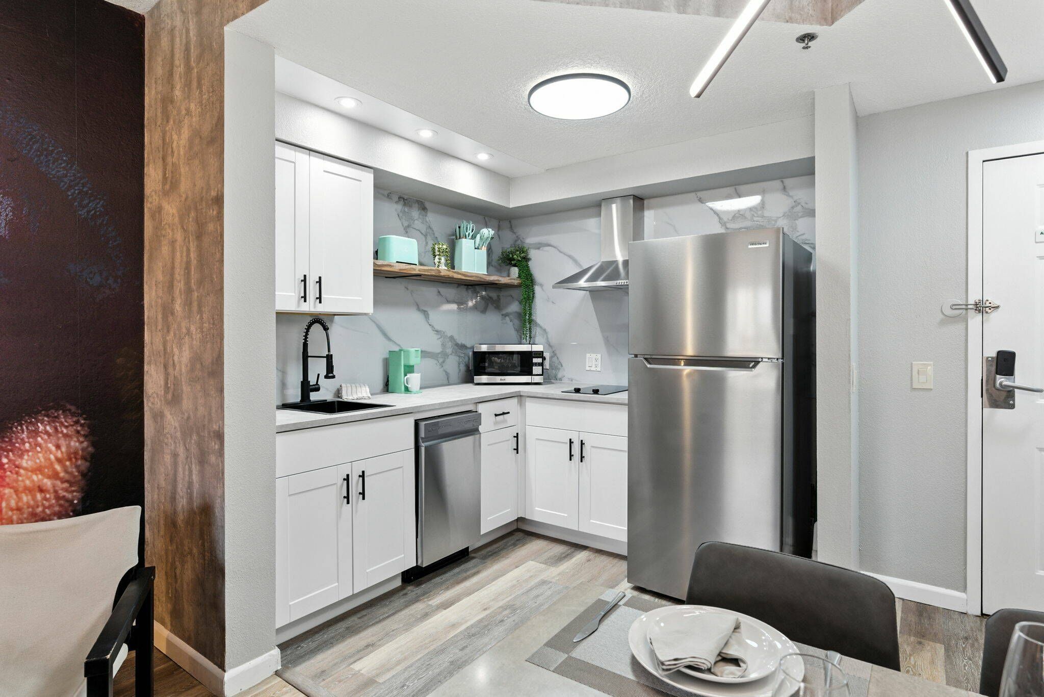 A modern kitchen with white cabinets, a stainless steel refrigerator, a microwave, and a dishwasher.