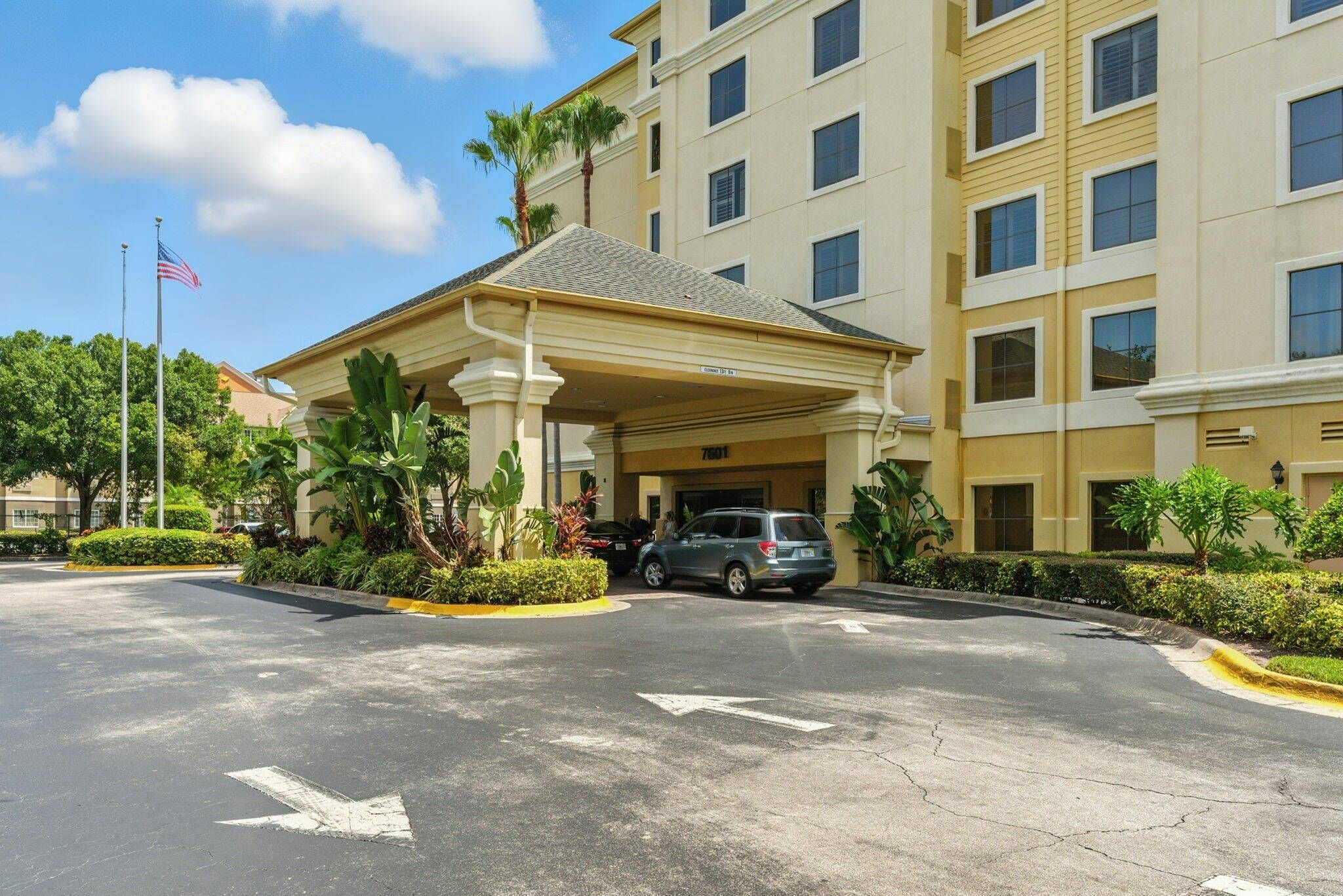 A hotel entrance with a covered parking area, a flag, and a building with multiple windows.