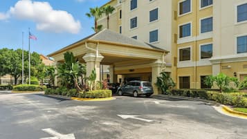 A hotel entrance with a covered parking area, a flag, and a building with multiple windows.