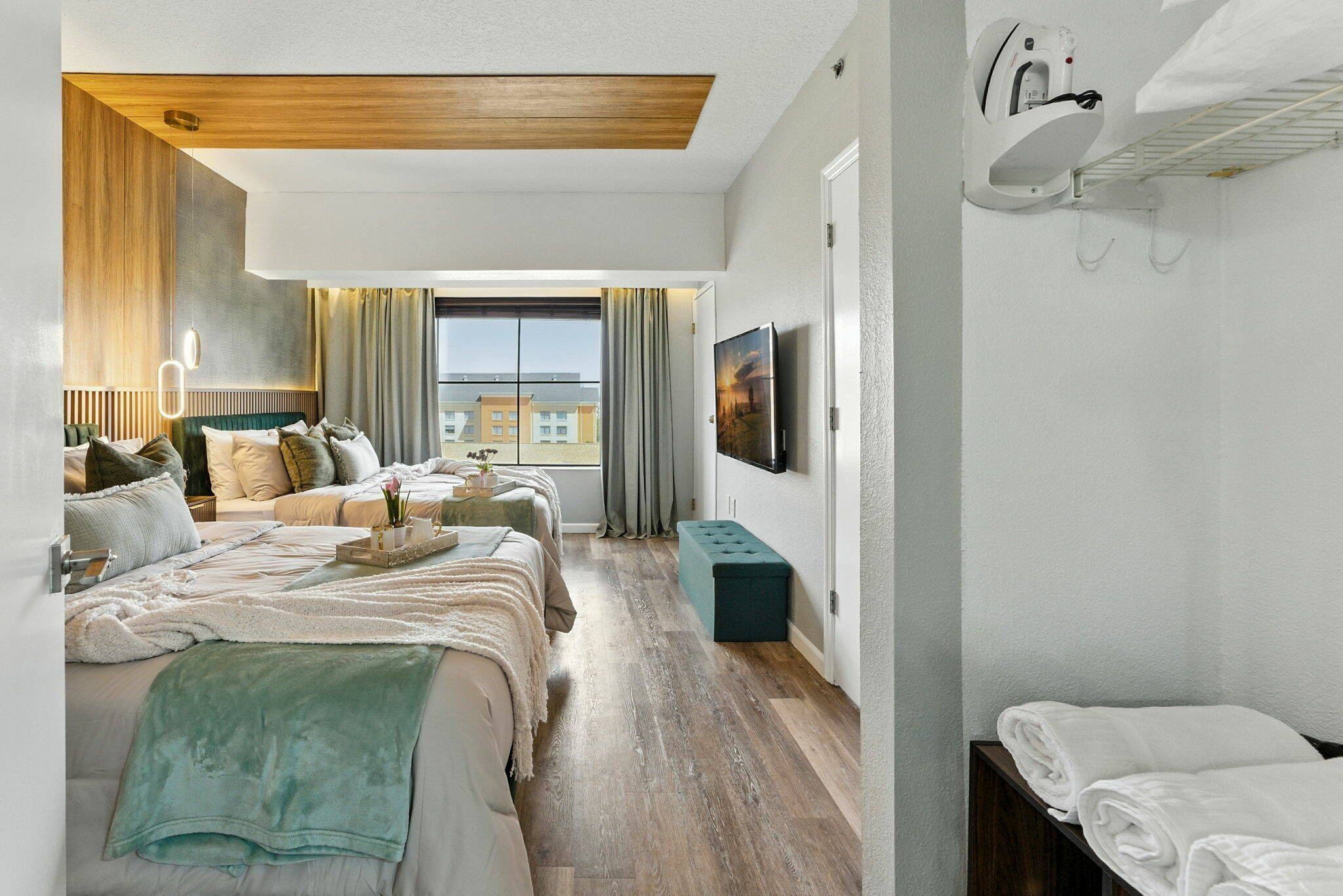 A hotel room with a large bed, a sofa, a TV, and a window with a view of buildings.