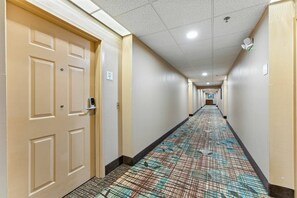 A hotel hallway with patterned carpet, beige doors, and a ceiling with recessed lighting. - 1BR ADA Apartment 5 min to Epic Universe (Orlando)