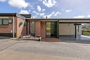 A modern building with a brick facade, a covered entrance, and a balcony with a railing. - Peaceful Upper Hutt Hideaway • Pool • Spa • Sauna (Upper Hutt)