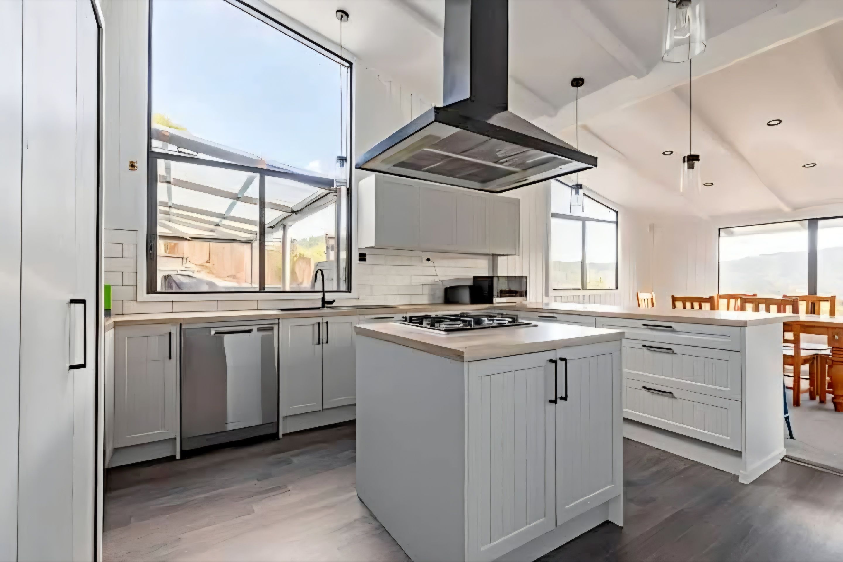 A modern kitchen with white cabinetry, a central island, and a large window providing natural light.