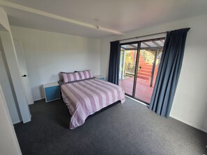 A bedroom with a bed, a nightstand, a drawer unit, and a sliding glass door leading to an outdoor area. - Peaceful Upper Hutt Hideaway • Pool • Spa • Sauna (Upper Hutt)
