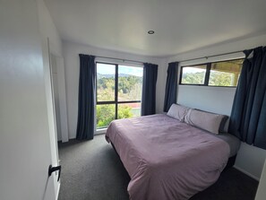 A bedroom with a large bed, a window with curtains, and a view of greenery outside. - Peaceful Upper Hutt Hideaway • Pool • Spa • Sauna (Upper Hutt)