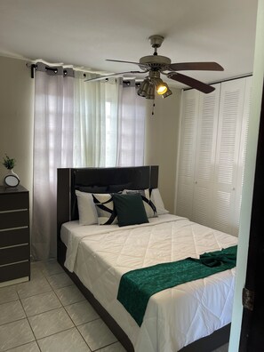 A bedroom with a bed, a ceiling fan, a dresser, and a window with curtains. - Cozy 2BR in Carolina 12min to Beach & Airport Near All (Carolina)