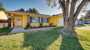 A yellow single-story house with a front porch, a large tree, and a well-maintained lawn. - Modern 4BR Sparks Retreat Hot Tub near Reno/Tahoe (Sparks)