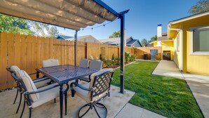 A covered patio with a table and chairs, a wooden fence, and a yellow building with a chimney. - Modern 4BR Sparks Retreat Hot Tub near Reno/Tahoe (Sparks)