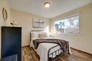 Ein Schlafzimmer mit Bett, Kommode, einem Fenster mit Blick und Wandbildern.