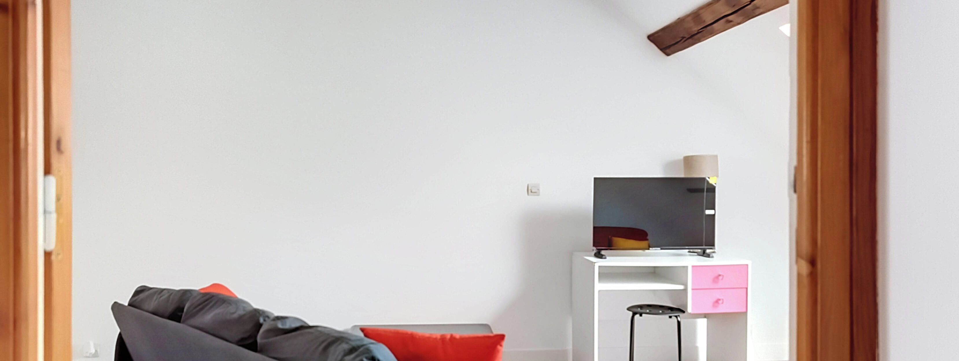 A room with a white desk, a chair, a sofa, and a small table with a lamp.