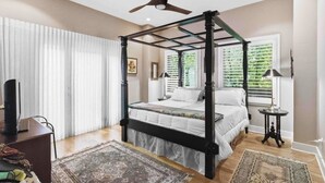 Ein Bett mit Baldachin, ein Deckenventilator, ein Fernseher auf einem Schreibtisch und ein kleiner Tisch mit einer Lampe.