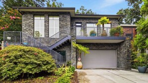 Ein modernes, zweistöckiges Haus mit Naturstein-Fassade, einer Garage und einem kleinen Balkon mit Blumentöpfen.