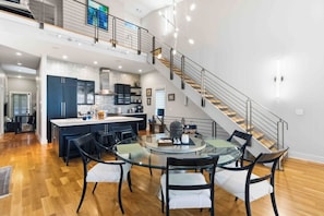 Cozinha ampla com ilha central, área de jantar com mesa de vidro e escada para o andar superior.