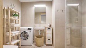 Une salle de bain moderne équipée d’un lave-linge, d’un évier, d’un miroir et d’une douche à parois de verre.
