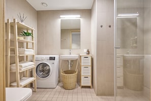 Ein modernes Badezimmer mit Waschmaschine, Waschbecken, Spiegel und einer Duschkabine.