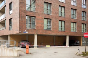 Un immeuble de plusieurs étages en briques, avec une entrée de garage, un panneau indiquant « Accès interdit » et une barrière de type « Videovalve ».