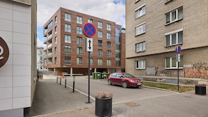Un immeuble résidentiel à plusieurs étages, avec une entrée de garage, un panneau indiquant qu’il est interdit de se garer et une voiture rouge stationnée devant.