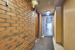 Un couloir avec un mur en briques, une porte dotée d’un panneau de verre et une entrée recouverte de moquette.