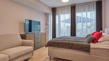 A modern hotel room with a bed, a sofa, a TV, and a window with curtains.