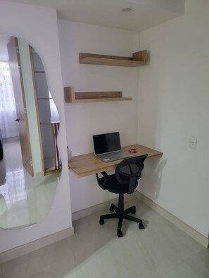 A room with a wooden desk, a black office chair, and a laptop. There are two wooden shelves above the desk.