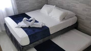 A double bed with white linens and a blue accent, positioned in a room with grey tiled walls and a wooden floor.