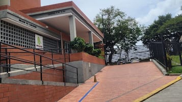 Un ingresso di un edificio con una rampa che conduce a un'area coperta, un percorso accessibile con sedia a rotelle e un vialetto recintato.