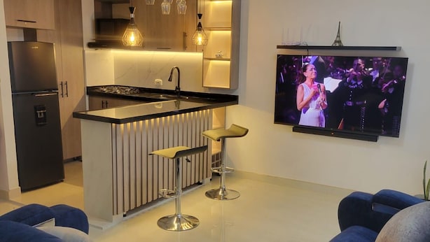 Una cocina moderna con una isla central, taburetes de bar y un televisor de pantalla plana montado en la pared.