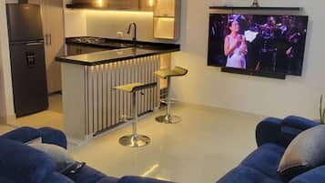 Une cuisine moderne dotée d’un îlot central, de tabourets de bar et d’un téléviseur à écran plat fixé au mur.