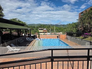 A swimming pool with a view of mountains, a covered seating area, and a fenced deck.
