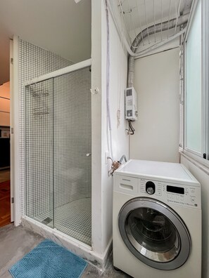 Une buanderie équipée d’un lave-linge, d’un sèche-linge et d’un espace douche fermé par des parois en verre.