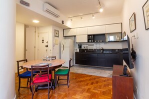 A compact kitchen with modern appliances, a dining area with a round table and chairs, and a small TV on a stand. - Copacabana Refuge Minutes From the Sea Jc602 (Rio de Janeiro)