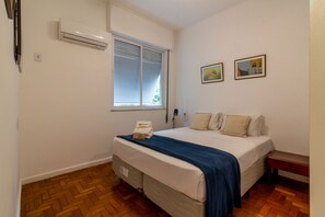 A bedroom with a bed, a window with blinds, a wall-mounted air conditioner, and two framed pictures. - Copacabana Refuge Minutes From the Sea Jc602 (Rio de Janeiro)