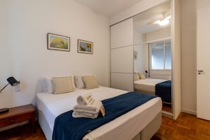 Une chambre d’hôtel avec un lit, une table de chevet, une lampe, un miroir et deux tableaux encadrés au mur.