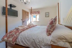 A bedroom with a four-poster bed, a flat-screen TV mounted on the wall, a window with a view, and a radiator.